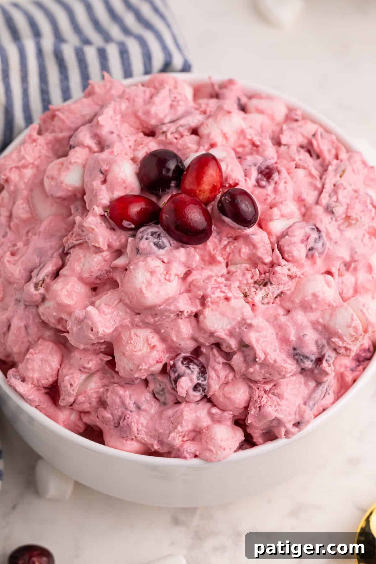 Cranberry fluff dessert salad in a white bowl with fresh cranberries on top.
