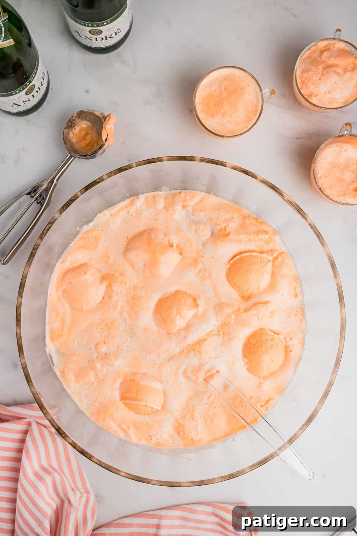 Sparkling Sherbet Punch 7 Orange sherbert champagne punch in glass bowl with glasses of punch, ice cream scoop, and bottles of champagne beside it.