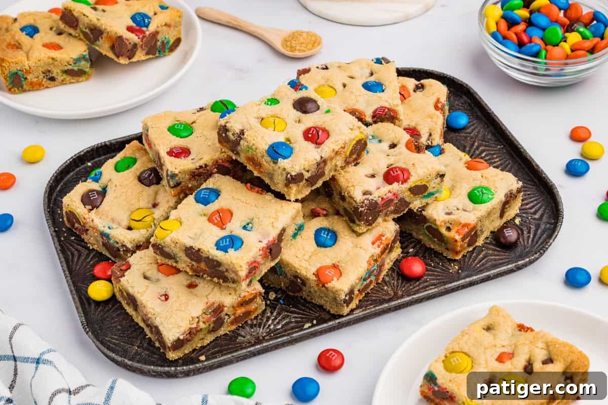 A stack of M&M cookie bars on a serving platter, surrounded by colorful M&M candies, creating an inviting and festive display.