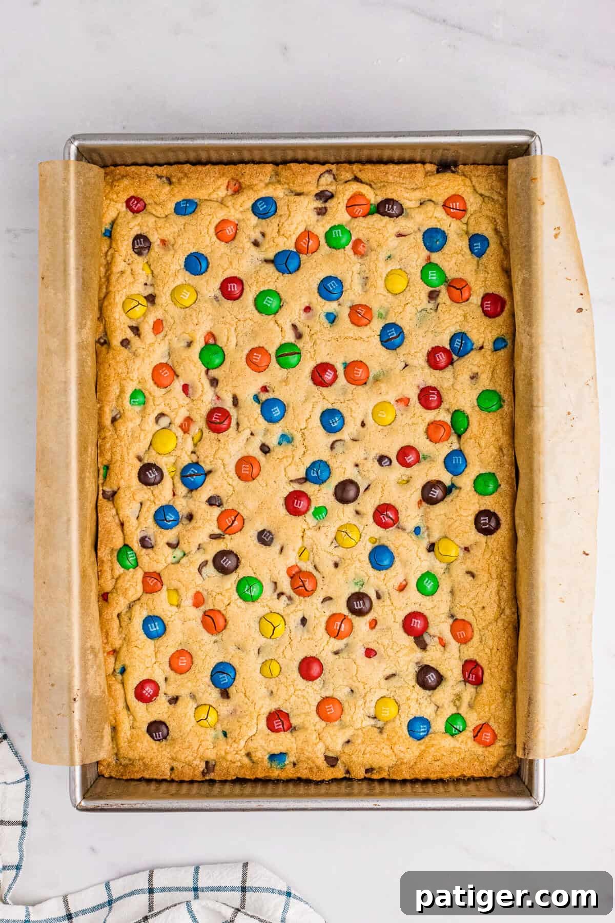 Freshly baked, golden brown M&M cookie bars, still warm and inviting in the 9x13 inch baking pan, with M&Ms slightly cracked on top.