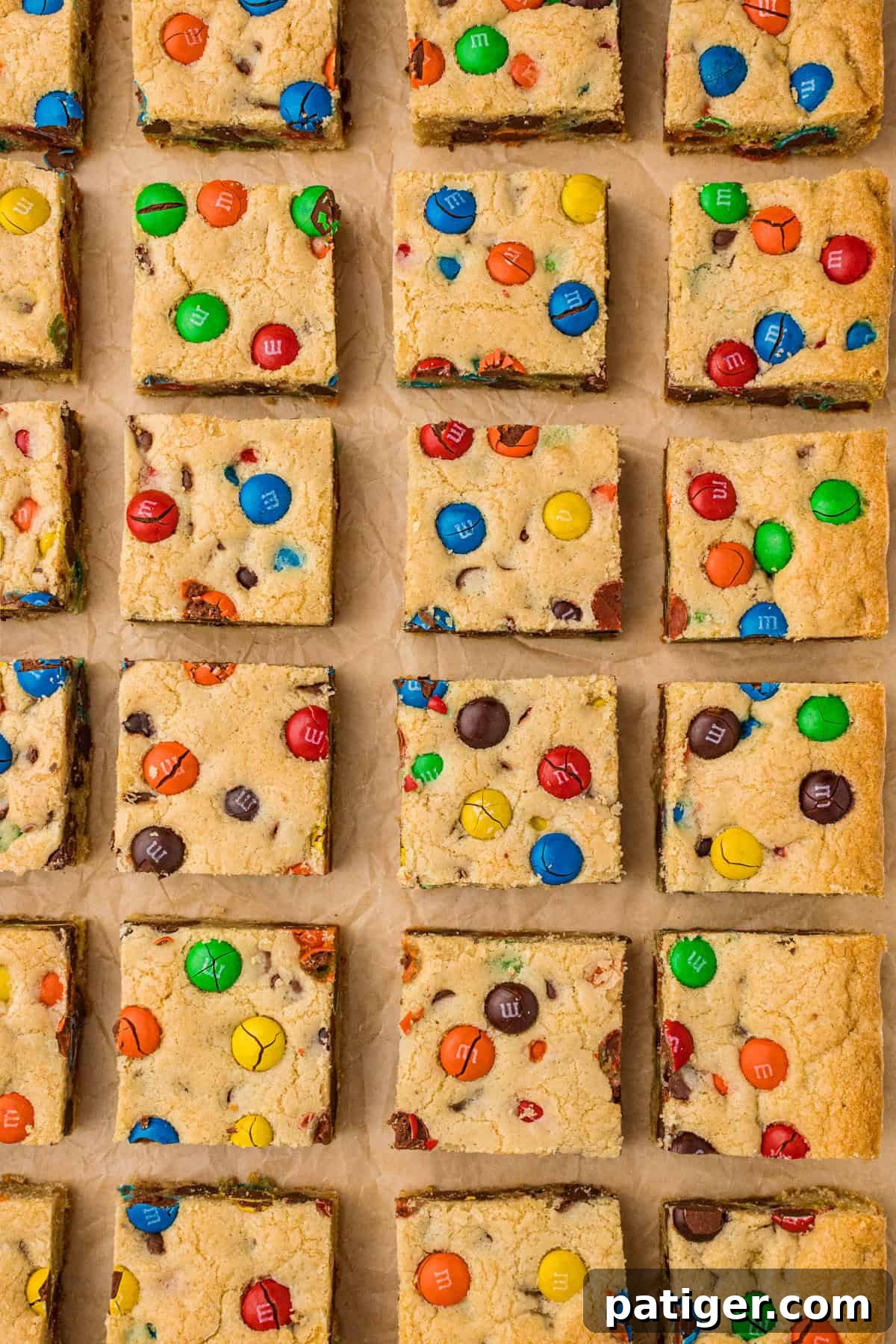 Finished M&M and chocolate chip cookie bars, beautifully sliced into neat squares and arranged on parchment paper, ready for serving.
