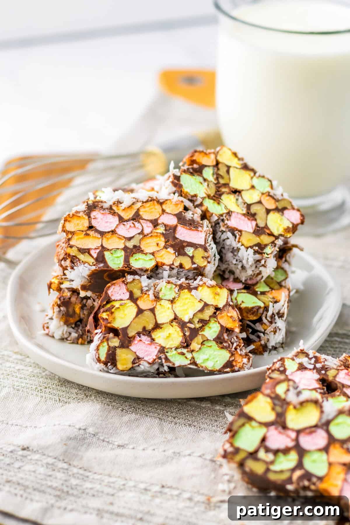 Stained Glass Cookies 3 Stained glass window cookies featuring vibrant marshmallow pieces and walnuts, wrapped in a rich chocolate and coconut layer, served on a plate alongside a glass of milk.