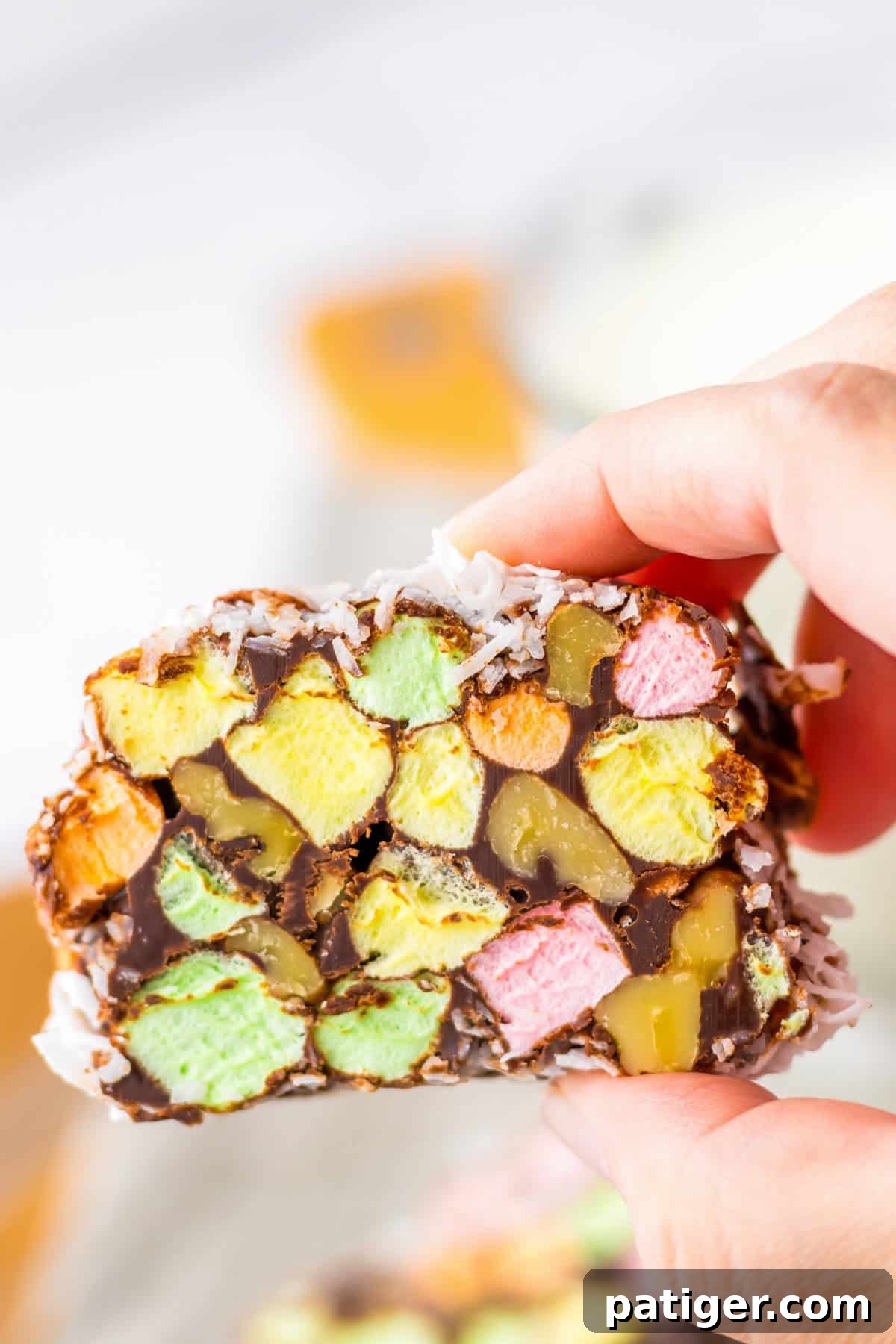 Stained Glass Cookies 7 Holding a no-bake church window cookie with bright marshmallow and nut centers, chocolate coating, and a coconut finish.