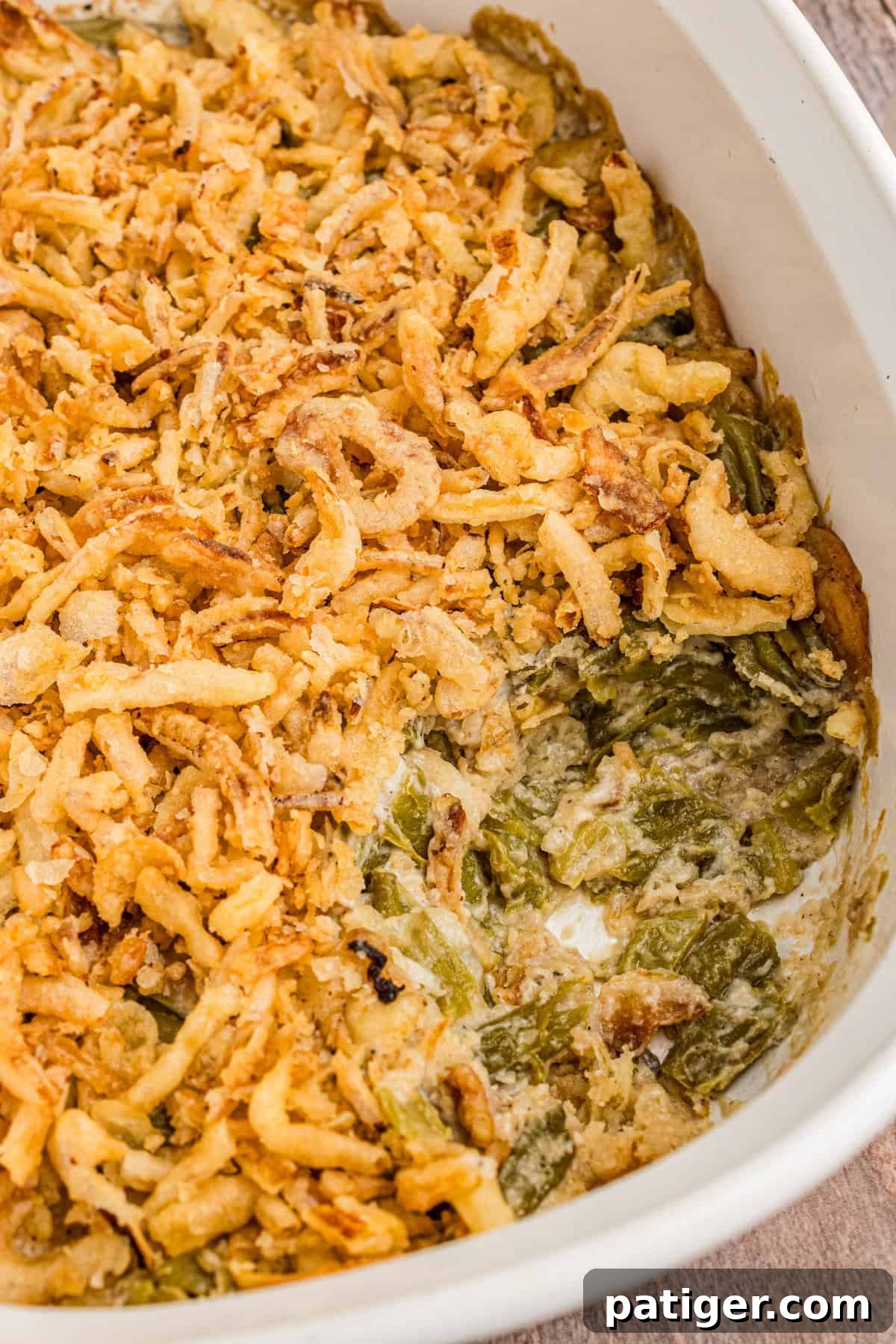 Creamy Green Bean Crunch 6 Casserole dish with green bean casserole made with Worcestershire sauce, cream of mushroom soup, and topped with crispy fried onions. A portion has been scooped out, revealing green beans in creamy sauce.