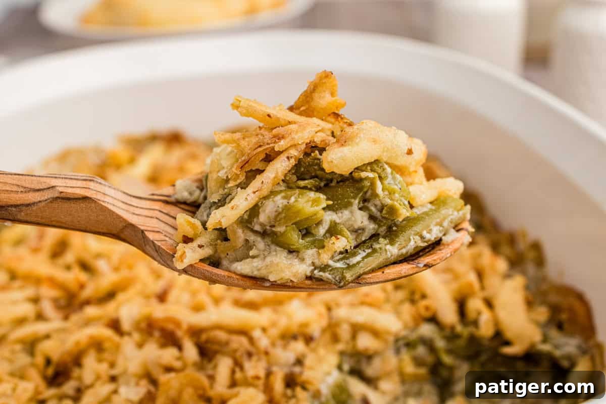 Creamy Green Bean Crunch 7 Classic green bean casserole topped with crispy fried onions, with a wooden spoon removing a portion from the dish.
