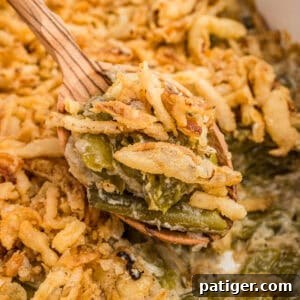 Creamy Green Bean Crunch 8 Spoonful of green bean casserole with Worcestershire sauce and crispy fried onions being served with a wooden spoon.