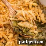 Creamy Green Bean Crunch 9 Spoonful of green bean casserole with Worcestershire sauce and crispy fried onions being served with a wooden spoon.