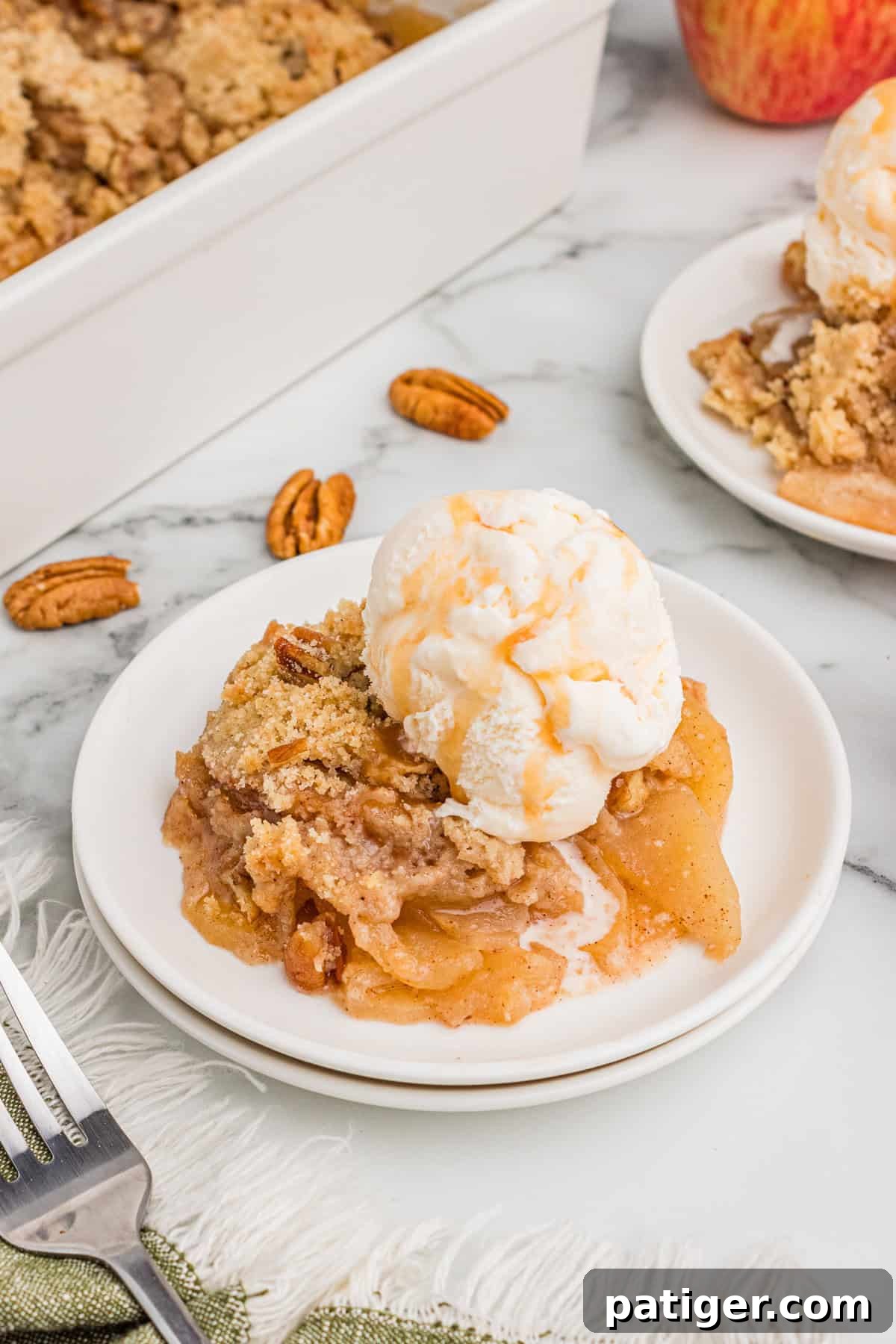 Apple crisp without oats served on a white plate, topped with a scoop of vanilla ice cream and drizzled with caramel sauce.