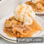 No oat apple crisp served on a white plate, finished with a scoop of vanilla ice cream and a drizzle of caramel sauce.