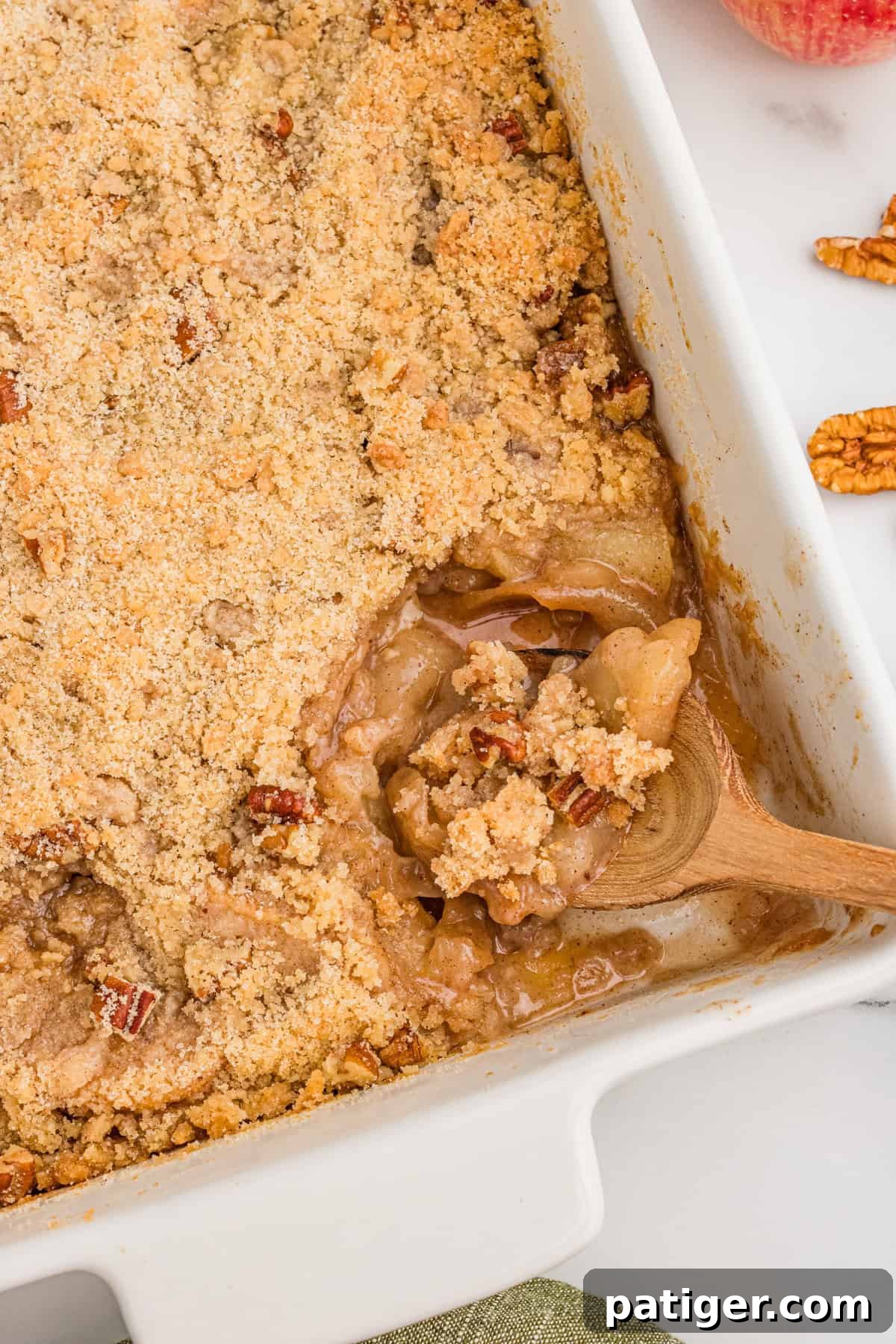 A wooden spoon scooping out a serving of apple crisp with no oat topping from a baking dish.