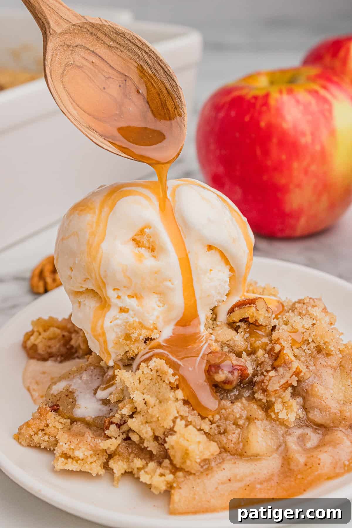 Close-up of caramel being poured over apple crisp, with fresh apples in the background.