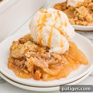 No oat apple crisp served on a white plate, finished with a scoop of vanilla ice cream and a drizzle of caramel sauce.