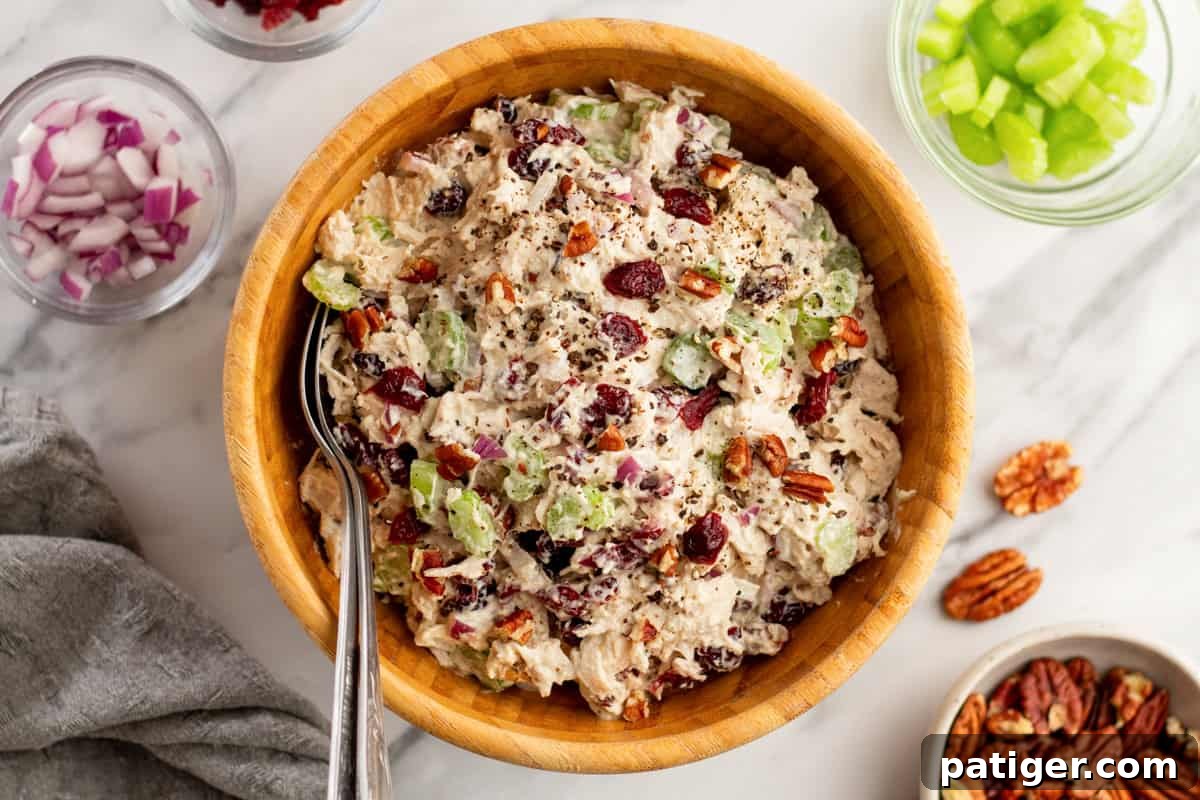 A vibrant display of Chicken Cranberry Salad with pecans, surrounded by its fresh ingredients: chopped red onions, crisp celery, and whole pecans, ready to be mixed.