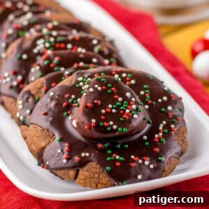 Cozy Hot Cocoa Cookies 11 Hot chocolate cookies topped with marshmallows, chocolate icing, and festive sprinkles on a white platter.
