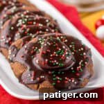 Cozy Hot Cocoa Cookies 12 Hot chocolate cookies topped with marshmallows, chocolate icing, and festive sprinkles on a white platter.