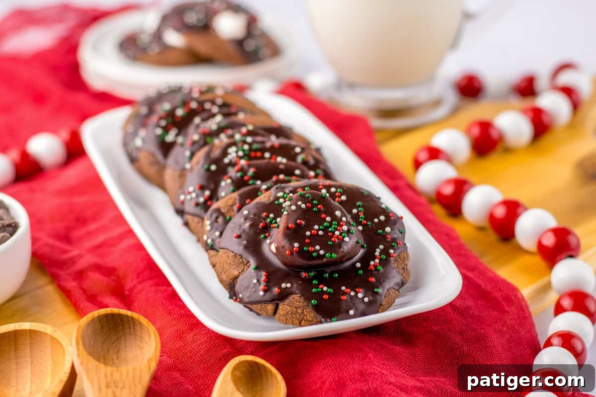 Cozy Hot Cocoa Cookies 10 Hot chocolate cookies with marshmallows, chocolate icing, and Christmas sprinkles on a white platter.