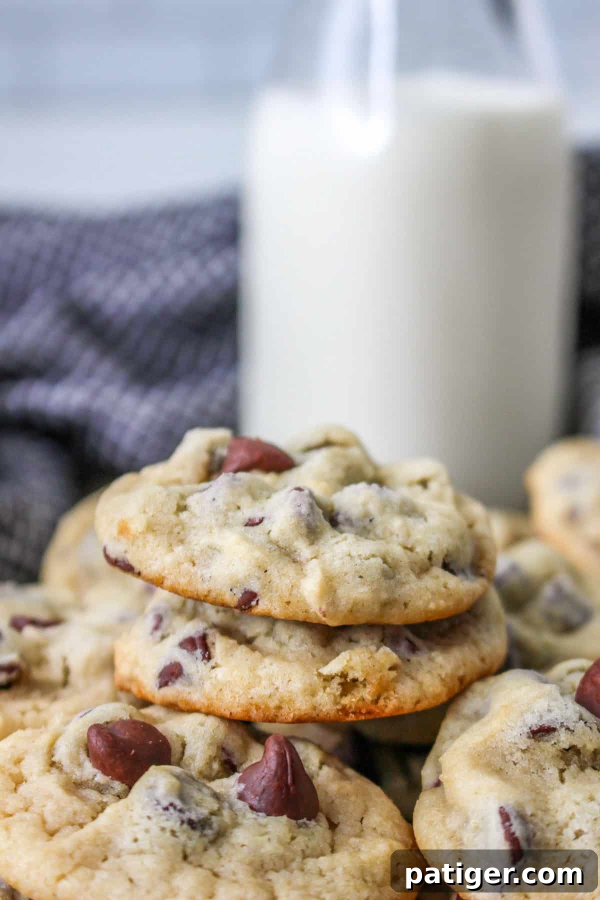 A close-up of a stack of soft and chewy yogurt chocolate chip cookies on a white plate, with a blurred glass of milk in the background, showcasing their perfect texture.