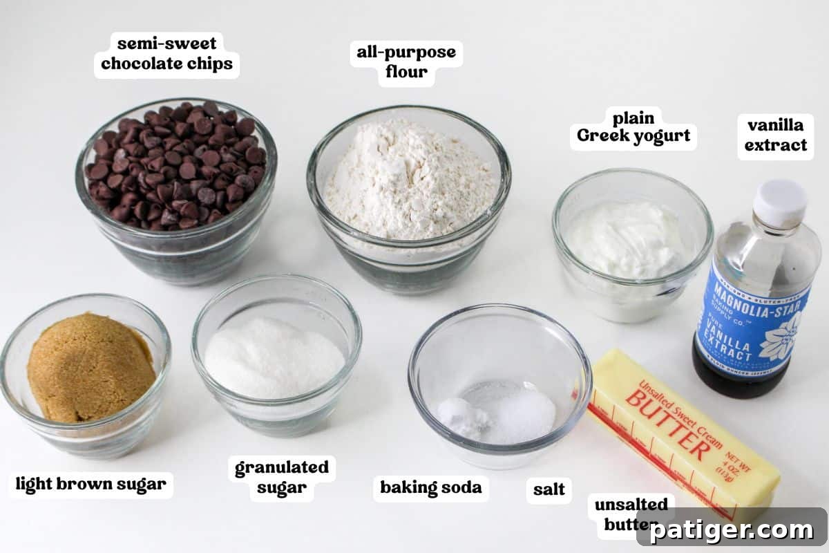 A collection of ingredients for baking Greek yogurt chocolate chip cookies, including unsalted butter, granulated sugar, light brown sugar, plain Greek yogurt, vanilla extract, all-purpose flour, baking soda, salt, and semi-sweet chocolate chips.