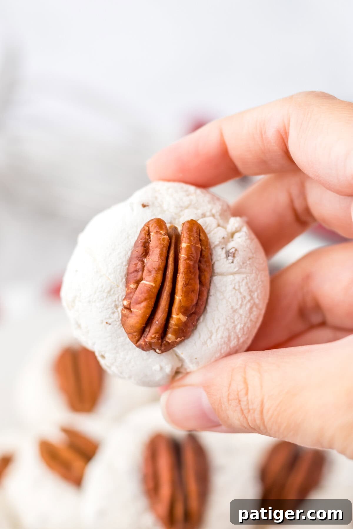 Close-up of a pecan-topped divinity cookie held in hand.