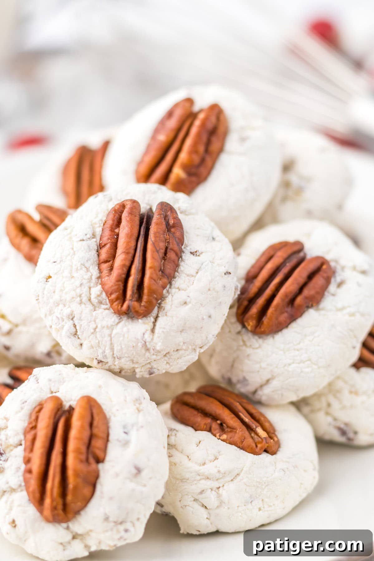 Close-up of pecan-topped divinity cookies piled on a white plate. showcasing the light, airy texture of this classic divinity candy recipe.