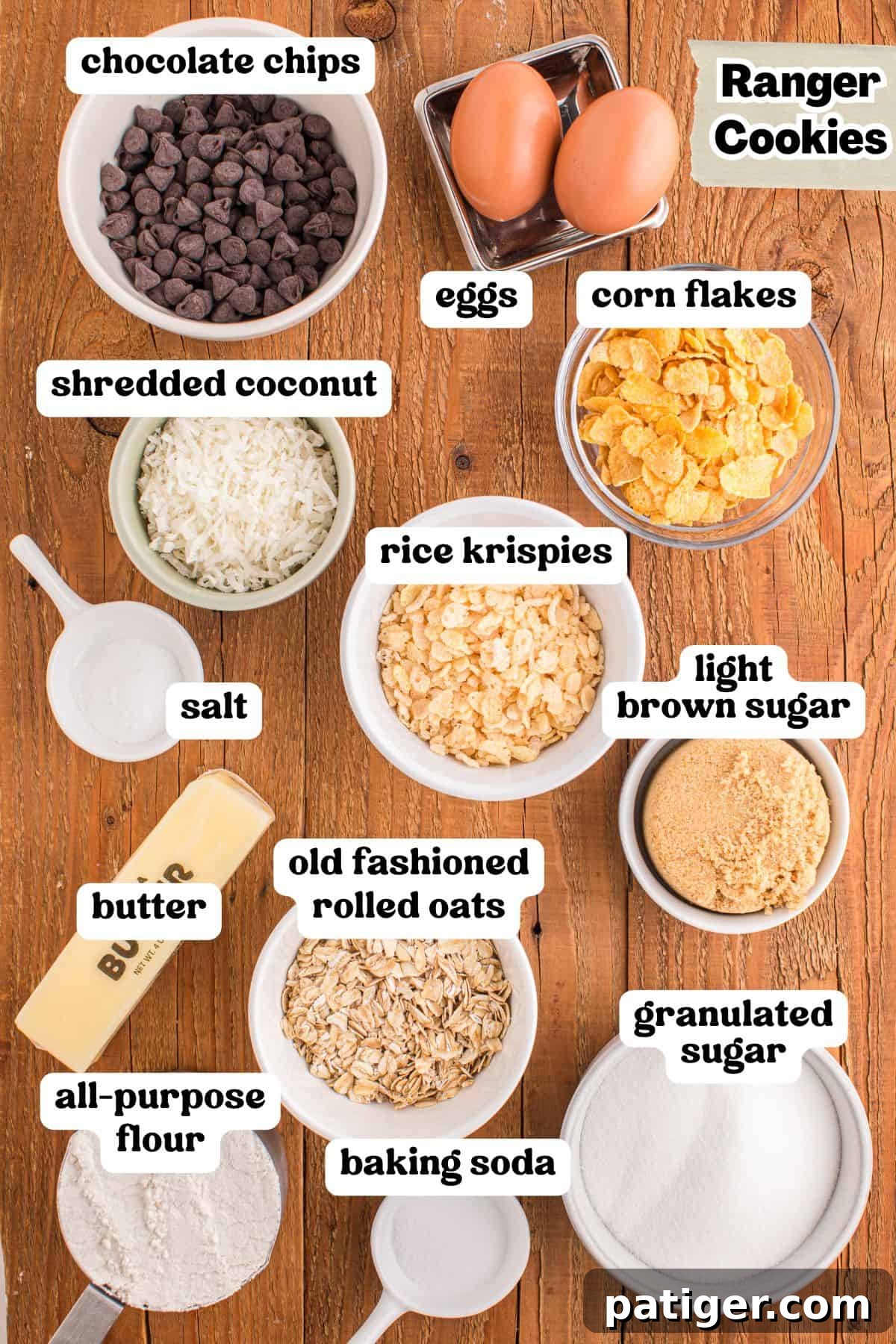 Flat lay of ingredients for Ranger Cookies on a wooden surface, including labeled bowls of chocolate chips, shredded coconut, rice krispies, corn flakes, light brown sugar, granulated sugar, old-fashioned rolled oats, all-purpose flour, baking soda, and salt, along with a stick of butter and two eggs, all perfectly prepped.