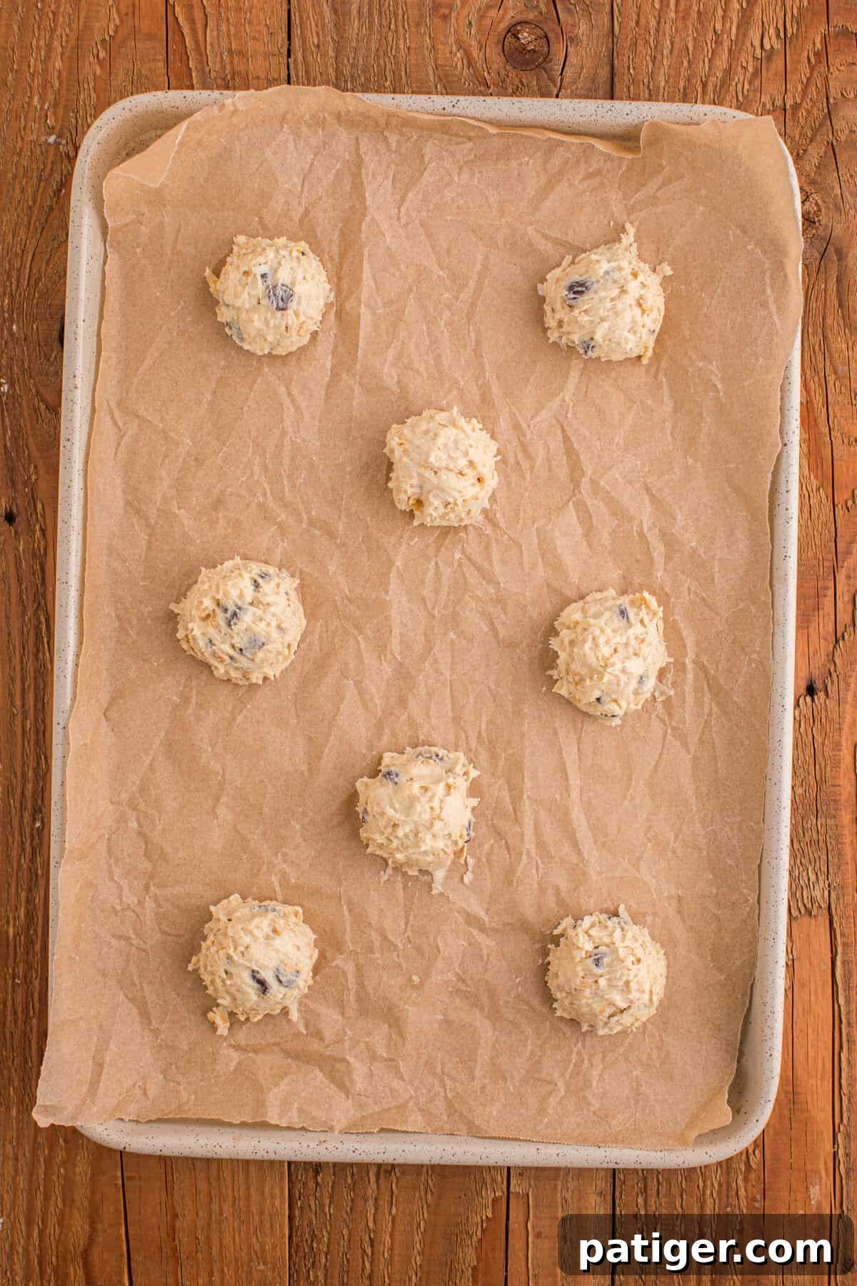 Baking tray lined with parchment paper and scooped cookie dough balls ready for the oven, surrounded by oats and cornflakes, showing perfect spacing for baking.