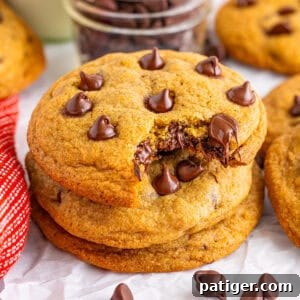 A stack of copycat Mrs. Fields chocolate chip cookies with one cookie bitten to reveal the gooey chocolate chips inside.