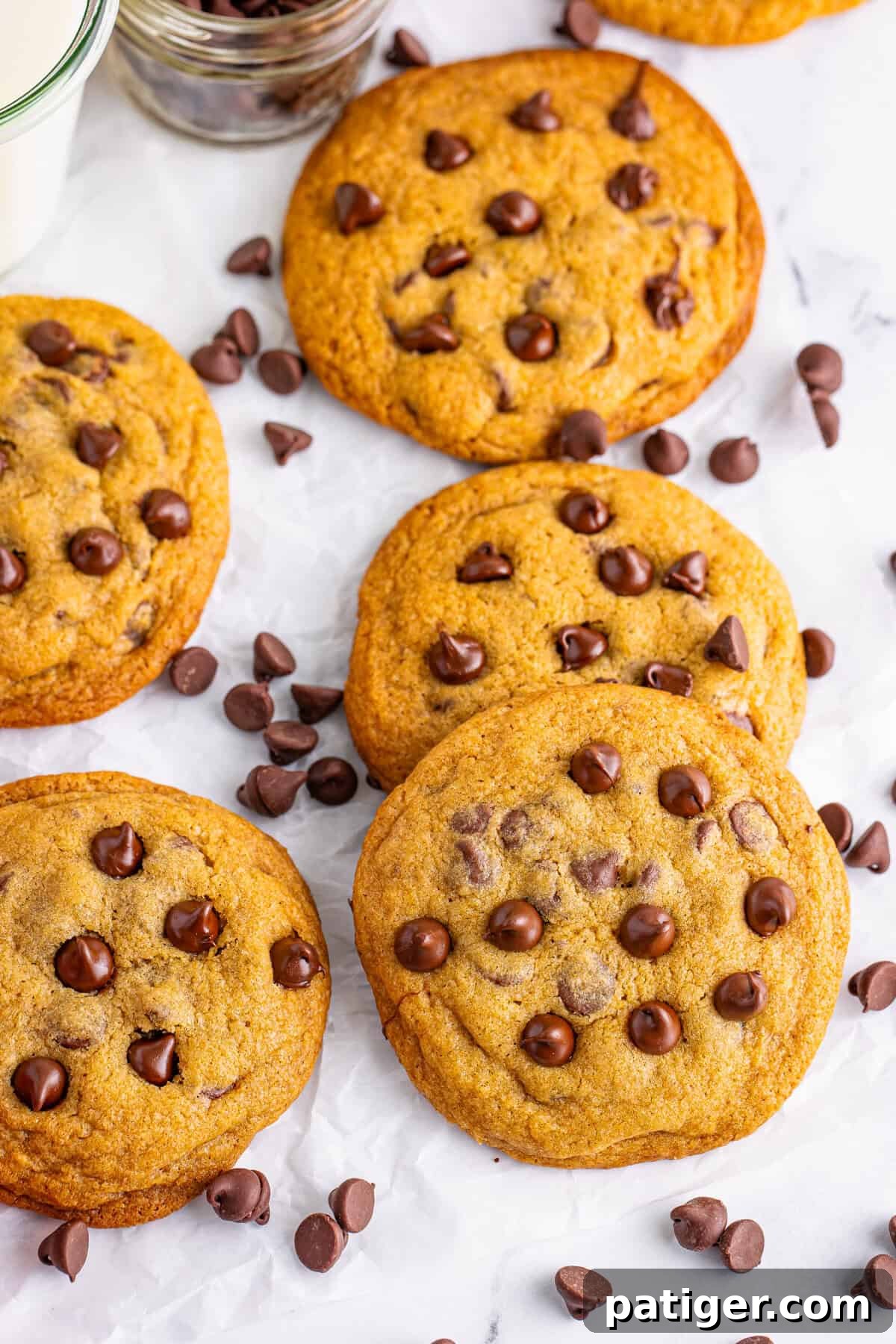A group of Mrs. Fields copycat chocolate chip cookies on parchment paper, surrounded by chocolate chips. These cookies are soft, chewy, and loaded with rich chocolate flavor.