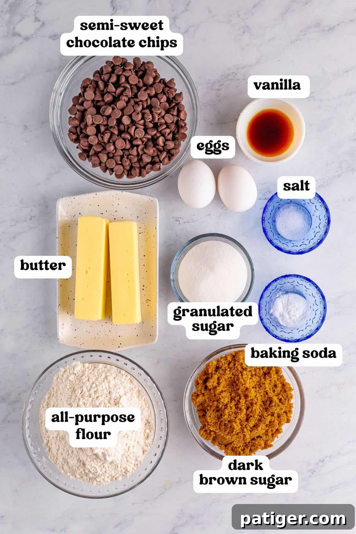 Ingredients for the Mrs. Fields chocolate chip cookie recipe, including semi-sweet chocolate chips, butter, eggs, sugar, flour, and vanilla, labeled neatly on a marble surface.