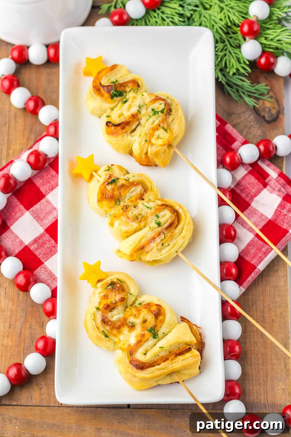 Golden-baked puff pastry Christmas trees with ham and cheese, garnished with parsley and cheddar stars, served on a white platter with holiday decor.