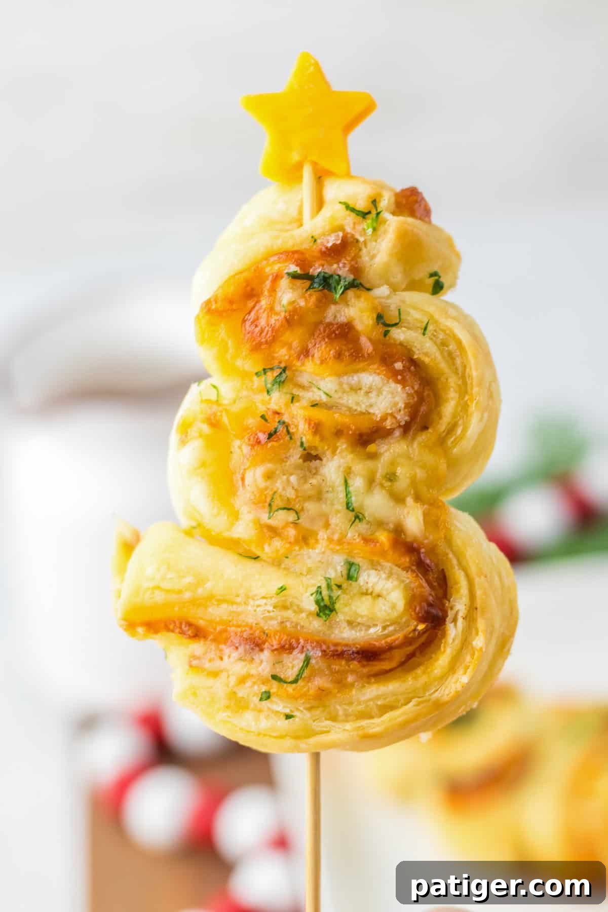 Single puff pastry Christmas tree appetizer on a skewer, showing layers of ham, cheese, and puff pastry topped with a cheddar star.