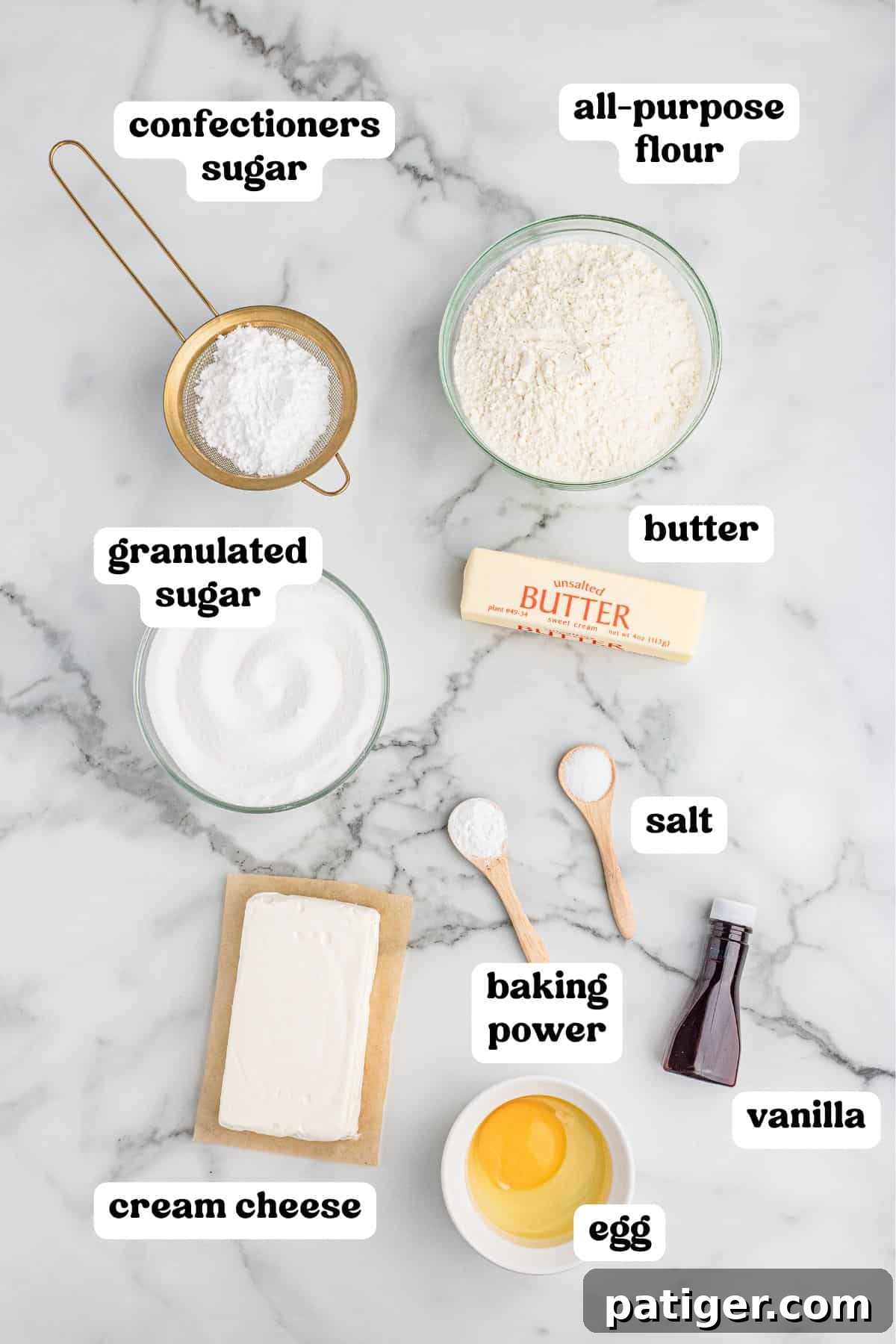 Velvety Cream Cheese Bites 3 Ingredients for cream cheese cookies on a marble surface, labeled: confectioners' sugar, all-purpose flour, granulated sugar, butter, cream cheese, salt, baking powder, vanilla, and egg.