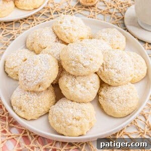 Velvety Cream Cheese Bites 9 A plate stacked with soft cream cheese cookies dusted with powdered sugar.