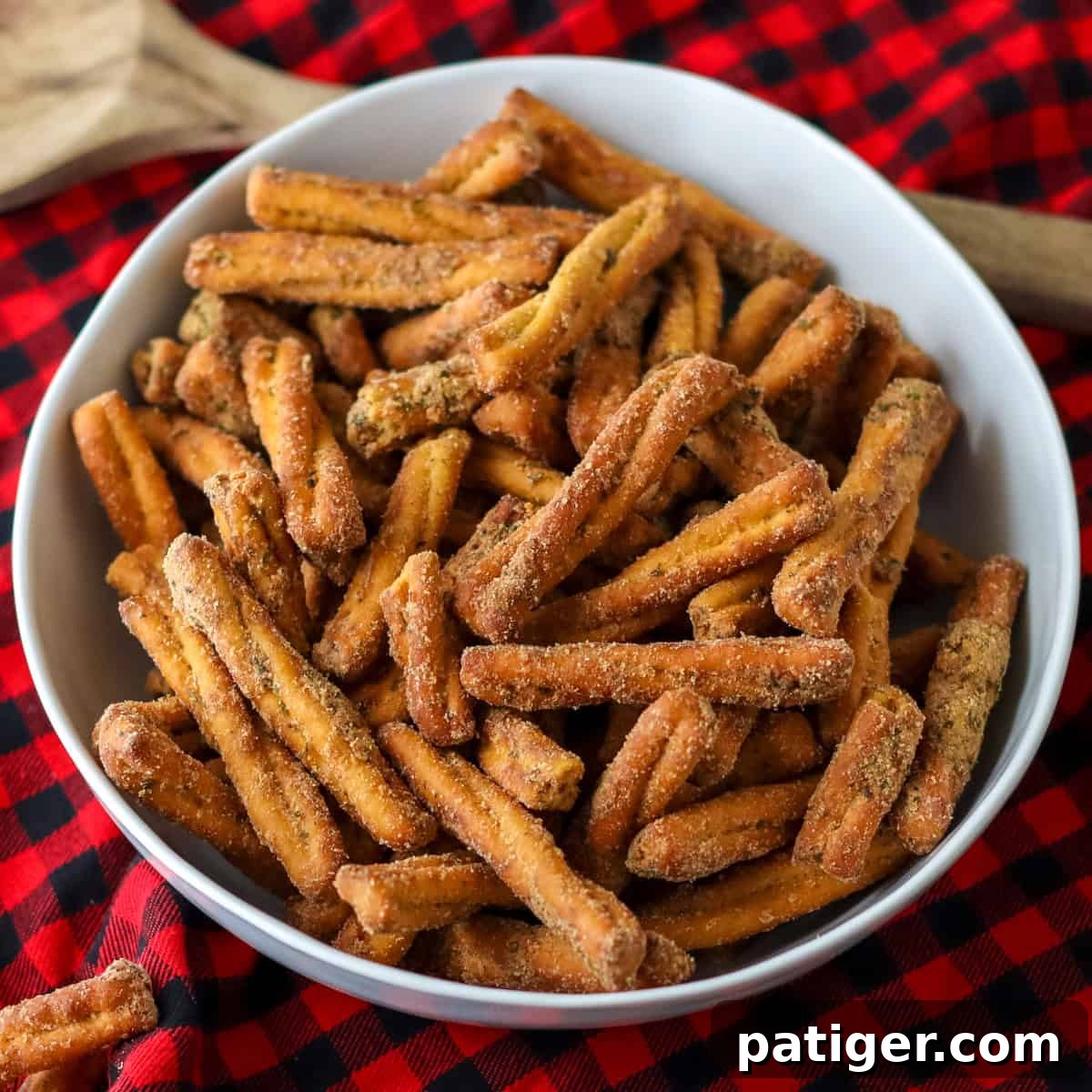 A bowl of golden-brown seasoned pretzel sticks, similar to Dot's pretzels, arranged invitingly on a classic red plaid background.