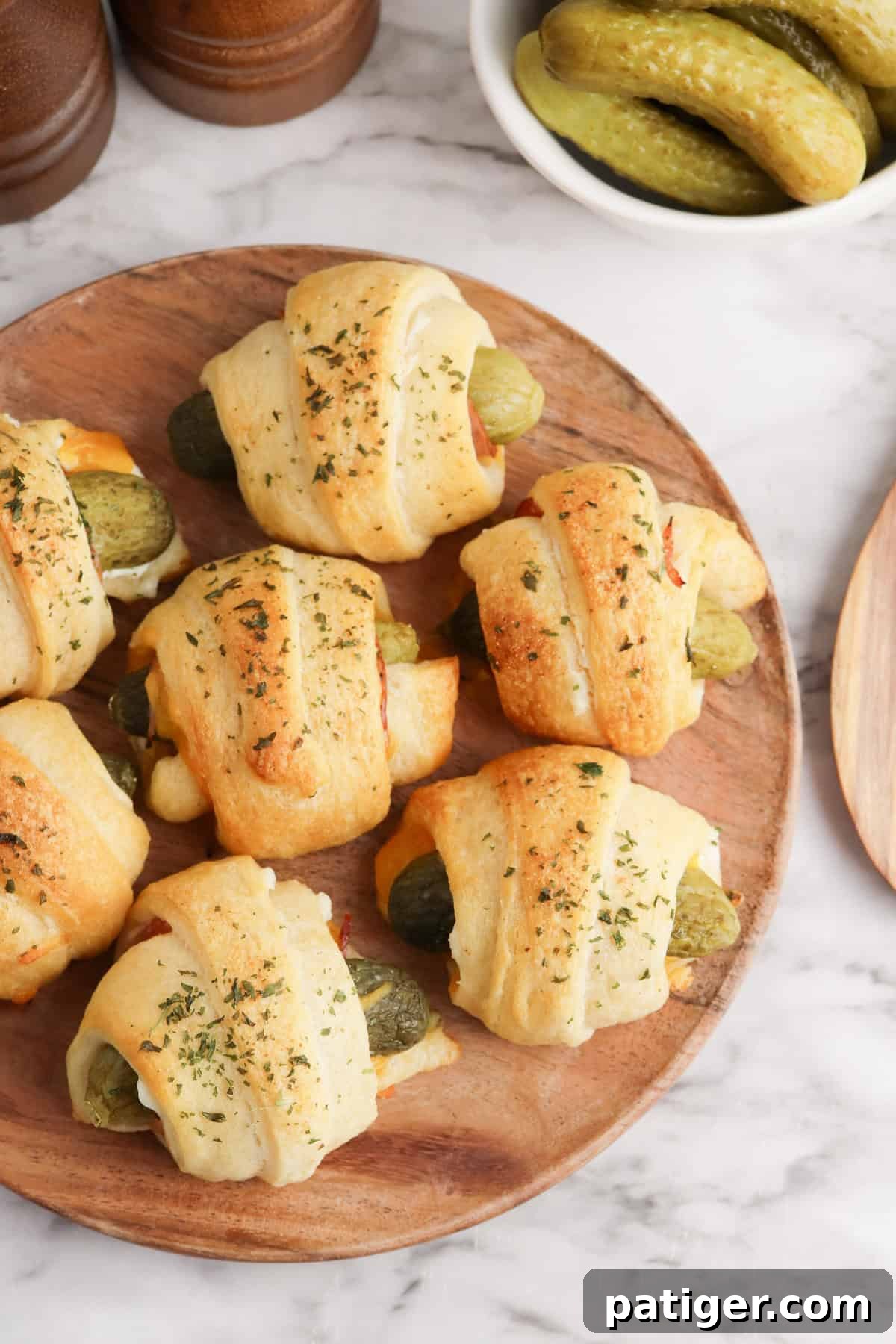 Dill Pickle Puffs 3 A plate with golden brown baked pickles in a blanket topped with herbs.