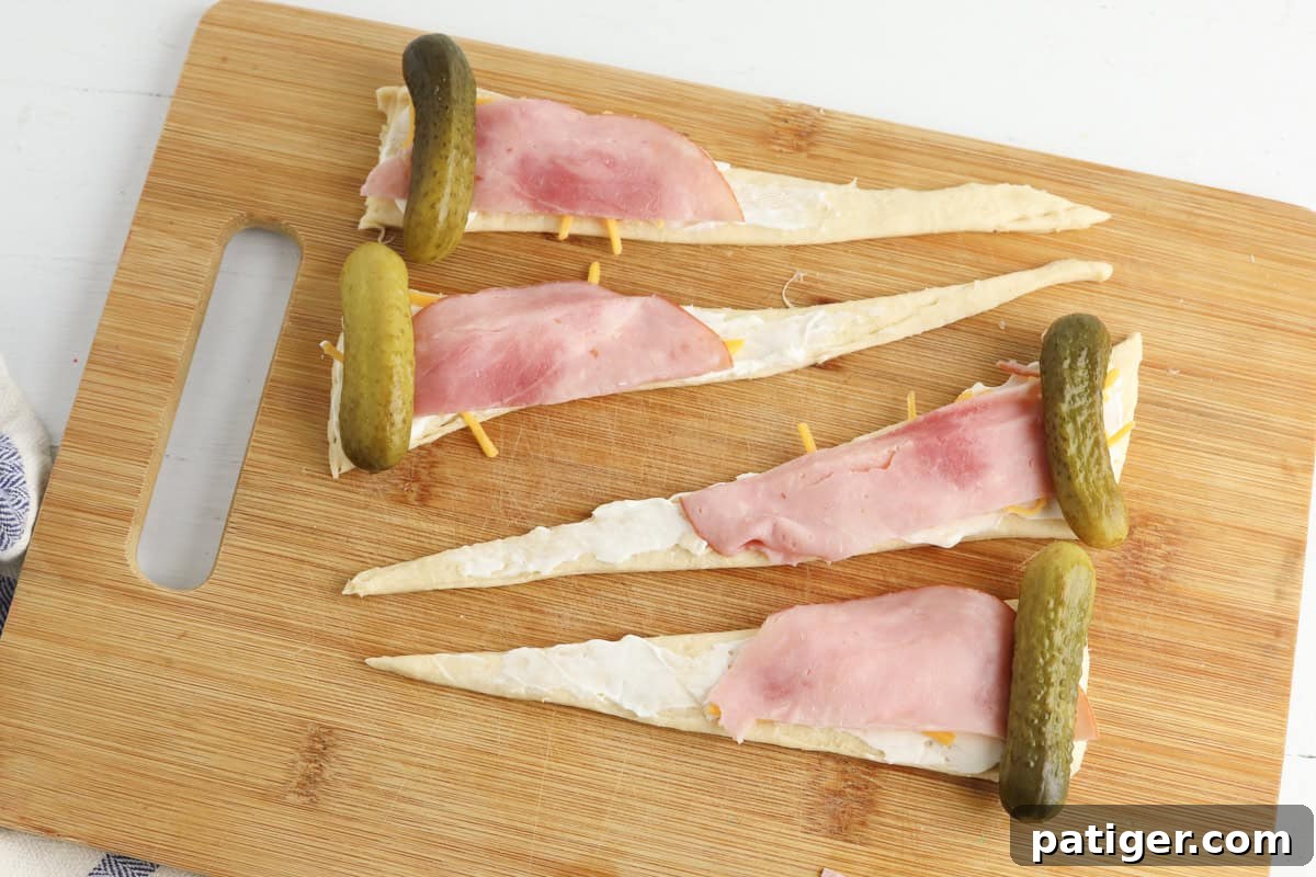 Dill Pickle Puffs 6 Each triangle is spread with cream cheese, topped with shredded cheddar, a slice of ham, and a whole pickle placed at the widest end.