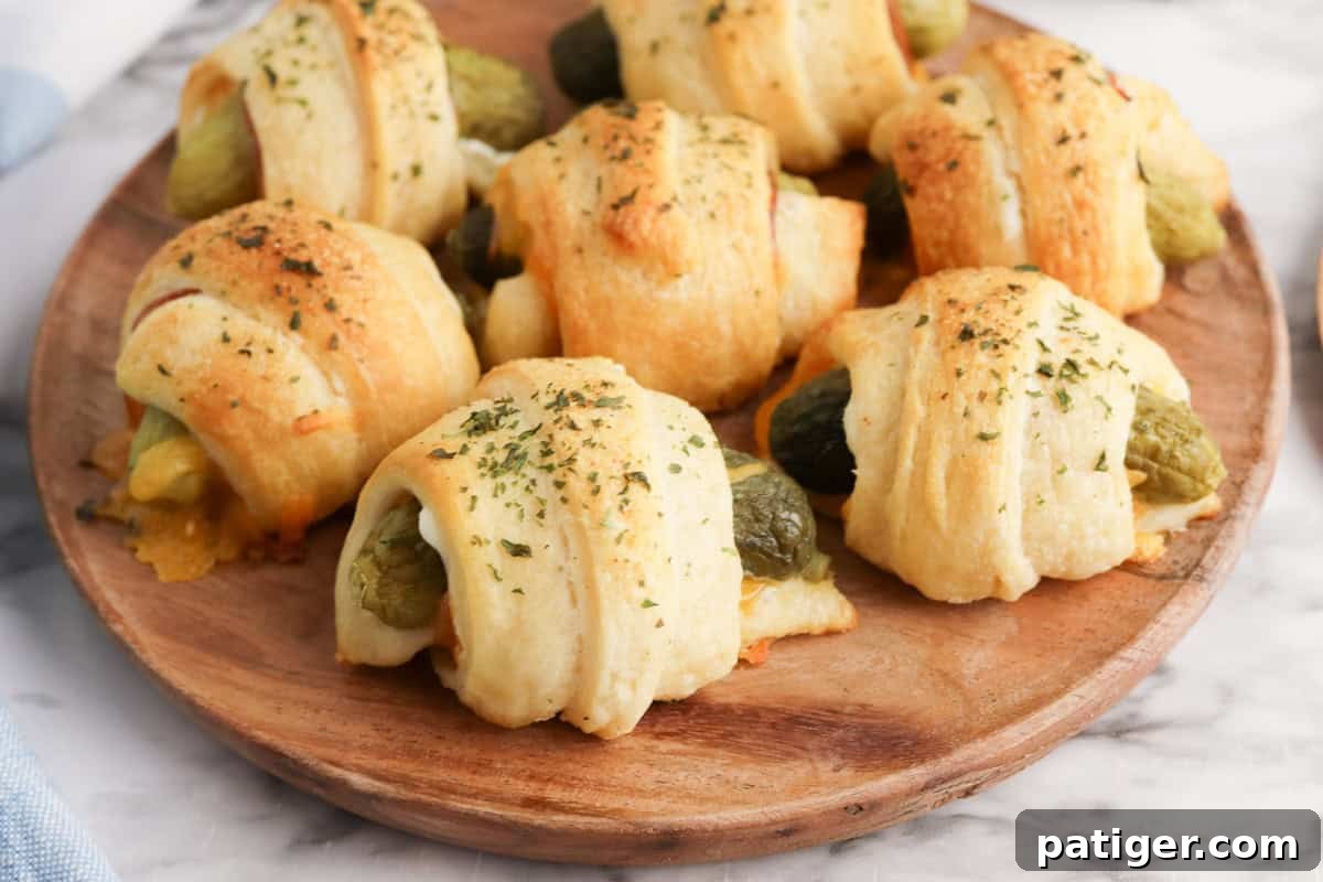 Dill Pickle Puffs 10 A close-up view of crescent roll-wrapped pickles on a round wooden plate. The rolls are golden and sprinkled with dried herbs