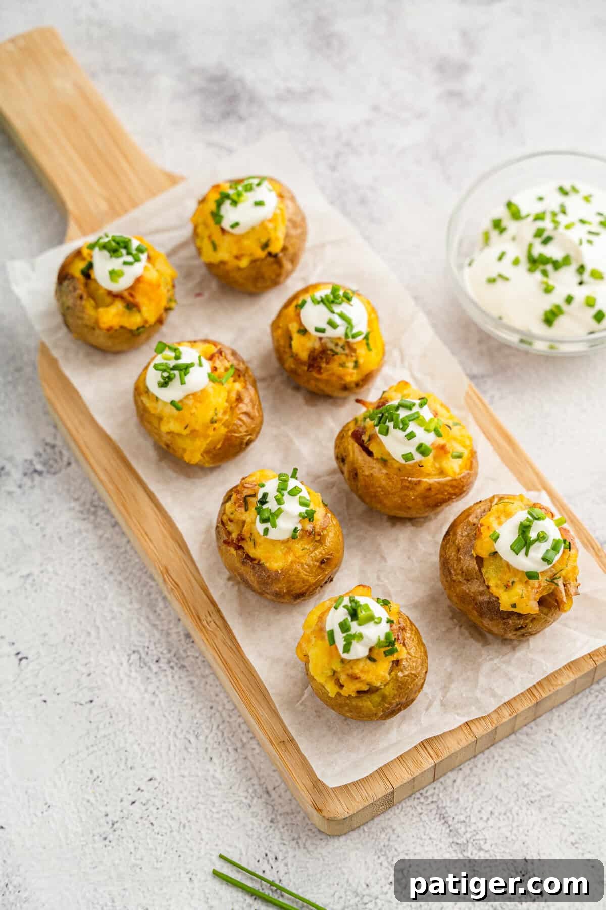Loaded Potato Bites 2 Bite-sized mini loaded potatoes arranged on a wooden serving board and topped with sour cream and chives, perfect for an appetizer.