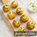 Bite-sized mini loaded potatoes arranged on a wooden serving board as an appetizer.