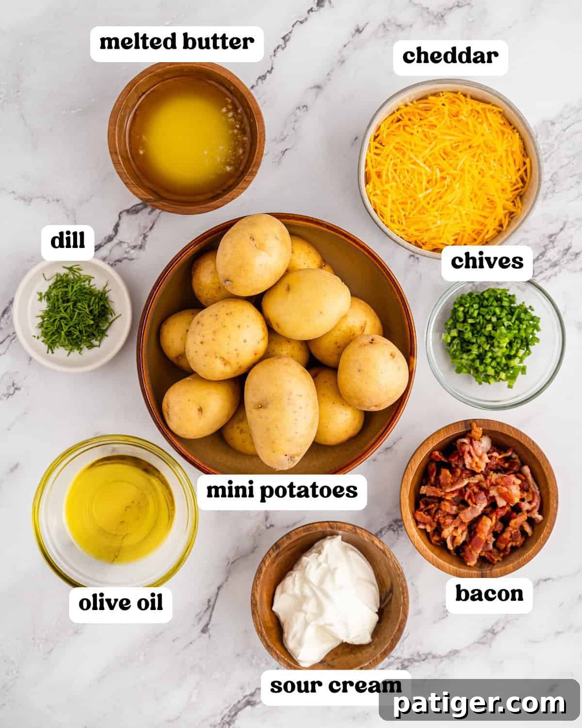 Loaded Potato Bites 4 Overhead view of all the ingredients needed for loaded mini baked potatoes displayed on a pristine marble surface. Items include vibrant mini potatoes, shredded cheddar cheese, crispy bacon pieces, creamy sour cream, fresh chives, aromatic dill, glistening olive oil, and rich melted butter, each ingredient clearly identifiable.