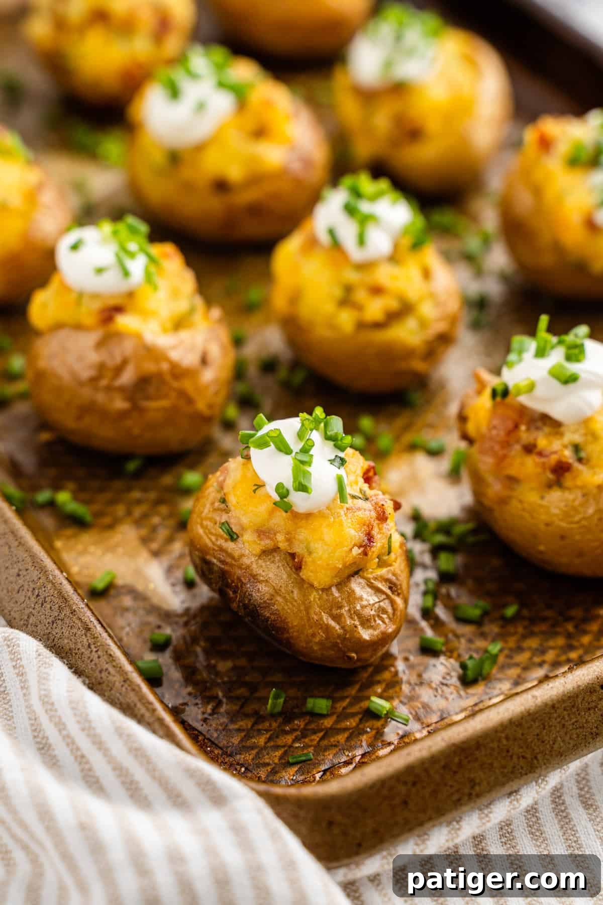 Loaded Potato Bites 9 A close-up of beautifully baked mini loaded potatoes on a baking sheet, featuring golden, crispy skins, a rich and creamy mashed potato filling, and elegantly garnished with dollops of sour cream and a sprinkle of vibrant chopped chives.