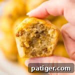 A hand holding a mini sausage pancake muffin with a bite taken out, revealing a fluffy interior with pieces of sausage. The background shows more sausage McGriddle bites stacked on a plate.