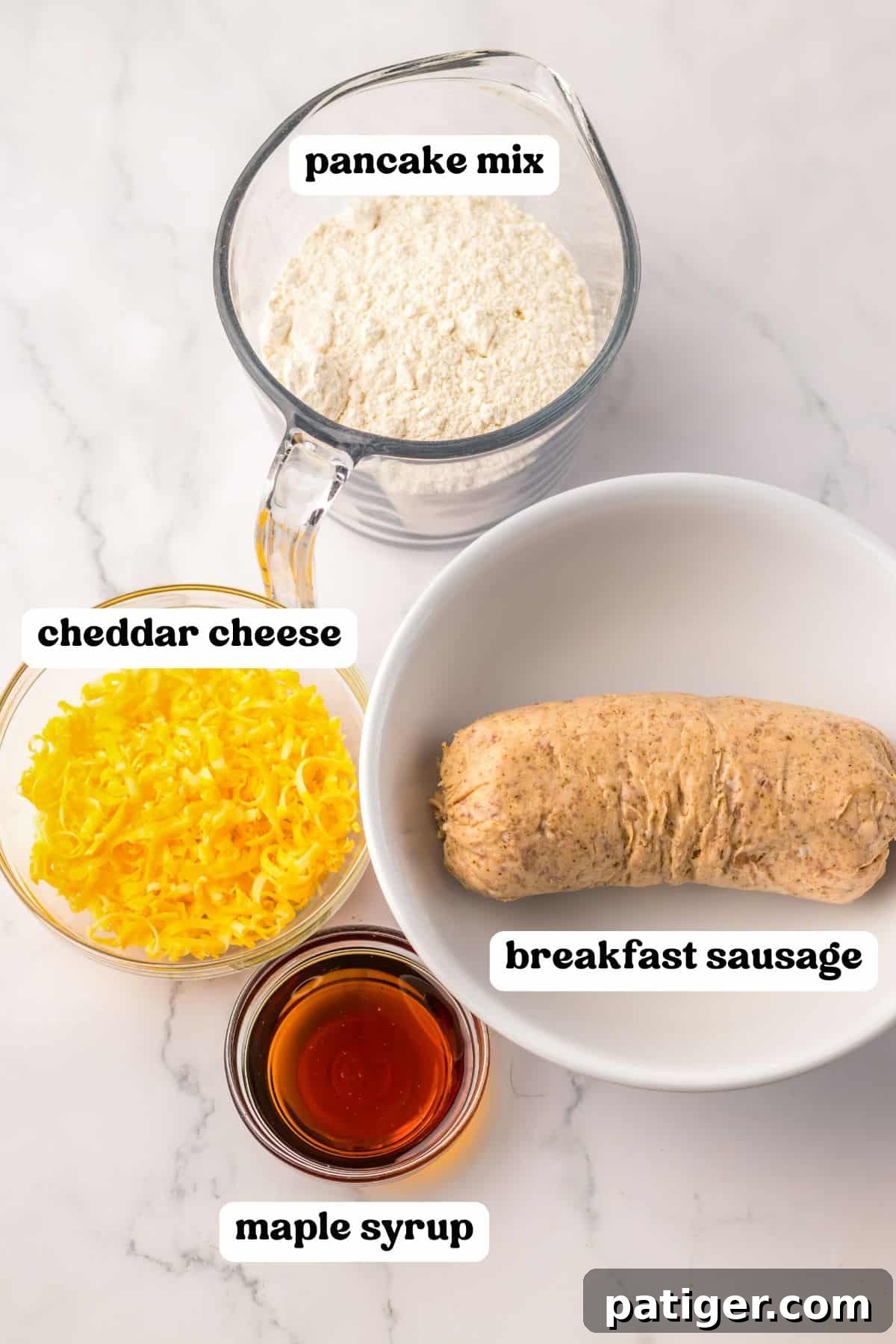 Four labeled ingredients for sausage pancake muffins: pancake mix, cheddar cheese, breakfast sausage, and maple syrup.