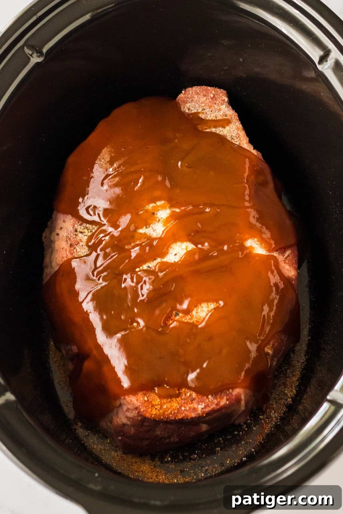 Melt-in-Your-Mouth Slow Cooker BBQ Beef 6 Seasoned chuck roast topped with BBQ sauce in a crockpot.