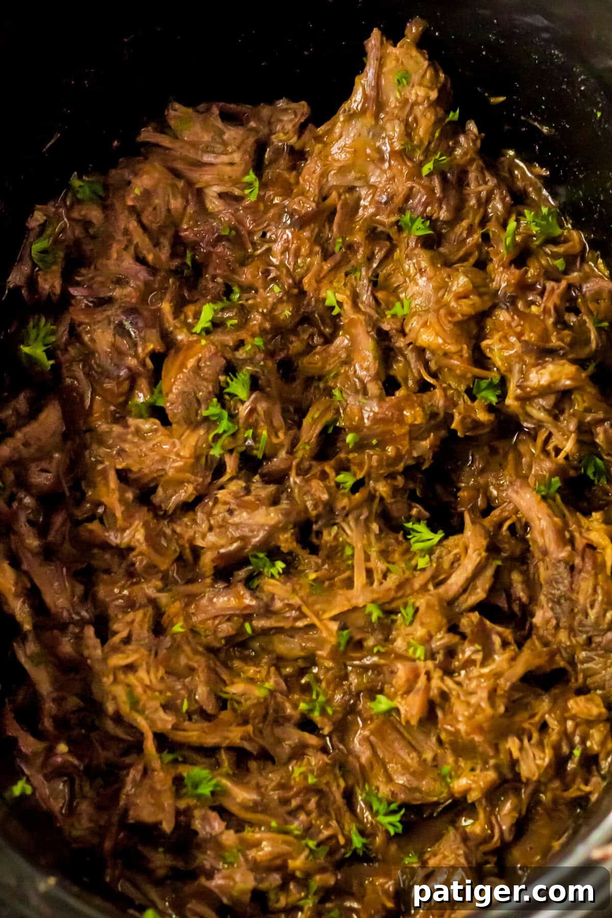Melt-in-Your-Mouth Slow Cooker BBQ Beef 7 Overhead image showing shredded BBQ beef filling the slow cooker, mixed with BBQ sauce and sprinkled with fresh chopped herbs.