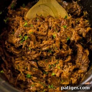 Melt-in-Your-Mouth Slow Cooker BBQ Beef 10 Close-up of shredded BBQ beef in a slow cooker, mixed with sauce and garnished with chopped green herbs. A wooden spoon is partially visible at the top.