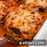 Close-up of a cheesy, golden-brown slice of baked eggplant Parmesan being lifted from a dish, revealing layers of eggplant and sauce with melted cheese on top, garnished with herbs.