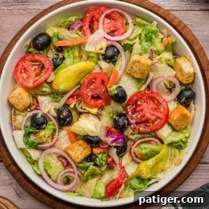 A top view of a bowl of copycat Olive Garden Salad with lettuce, tomatoes, olives, onions, croutons, and pepperoncini.