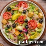 A top view of a bowl of copycat Olive Garden Salad with lettuce, tomatoes, olives, onions, croutons, and pepperoncini.