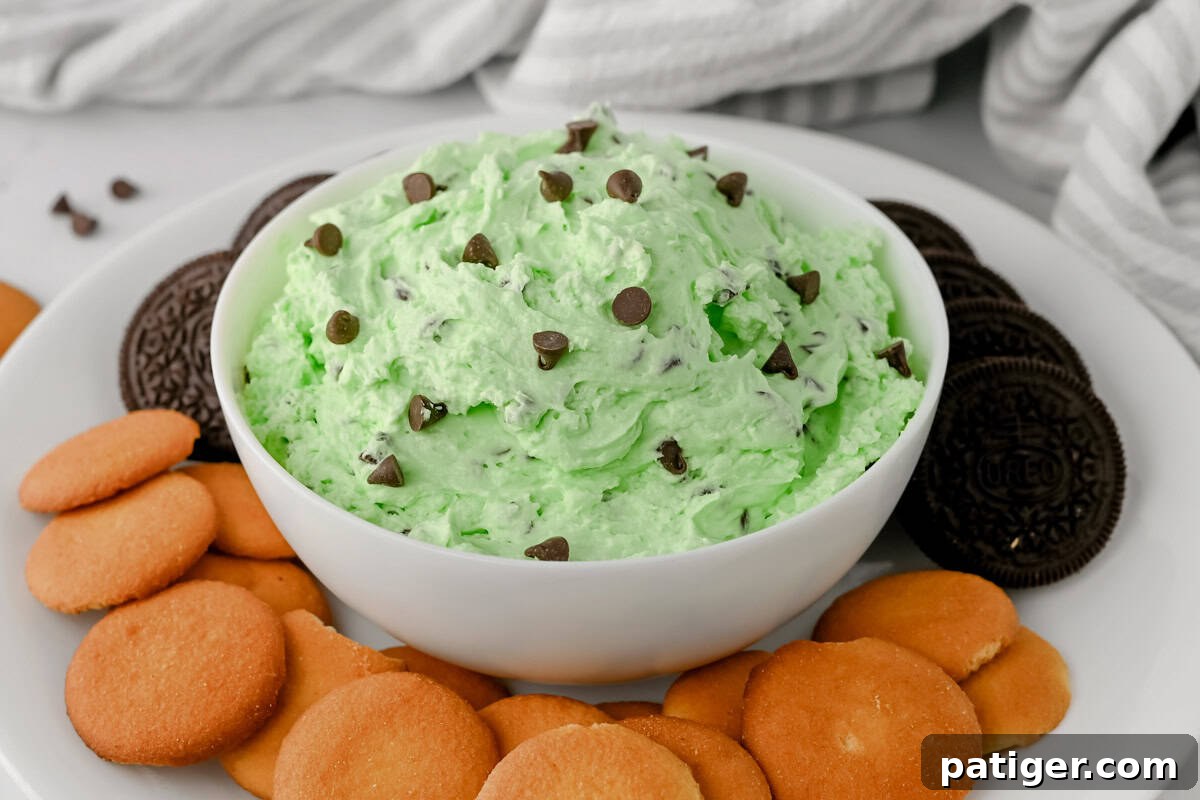 Bowl of mint chocolate chip dip topped with chocolate chips, surrounded by vanilla wafers and chocolate sandwich cookies.